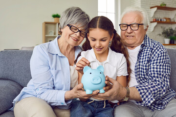 Loving grandparents help granddaughter save up money in piggy bank. Happy, smiling child girl...