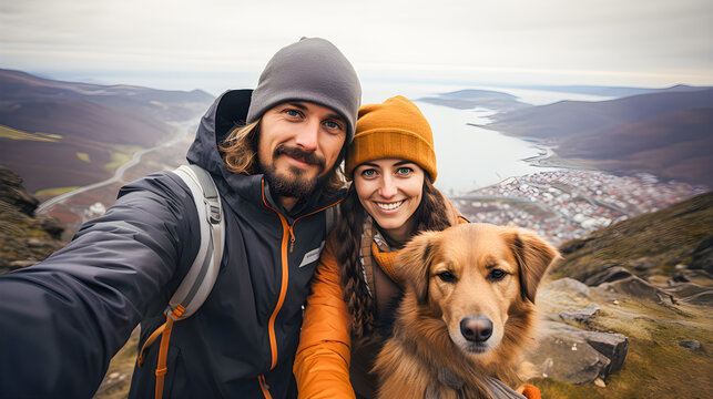Happy couple of hikers with their dog taking a selfie on the mountain dressed in hiking clothes.