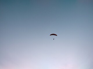 Paraglider flying on the parachute during sunset on the meadow.