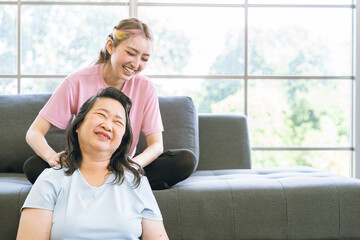 Fototapeta premium Asian mother fill happy that Cute Asian daughter sit on sofa and giving massages shoulder, relieves pain of elderly Asian mother at home.