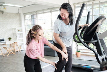 Fototapeta na wymiar Asian young lady trainer helping senior old lady having knee sprain or injury while workout or running on treadmill in gym. Workout trainer suggestion or consult in gym for reduce injury.