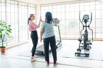 Cute young lady and senior old lady motivate each others by doing high five or touching hand before exercise with treadmill or running machine, Happy healthy workout with parent at home concept.