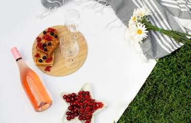 Romantic, summer picnic in park on the grass. Champagne and two glasses on white plaid. Concept of food and drink.
