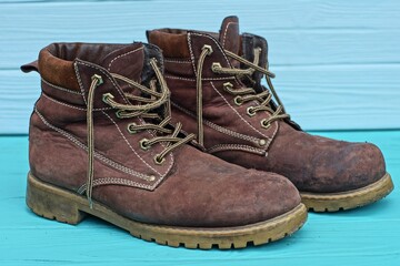 a pair of brown men's stylish winter model old leather lace-up comfortable warm boots stands on a green wooden table