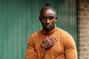 Fit black male model with hand on chest outdoors.