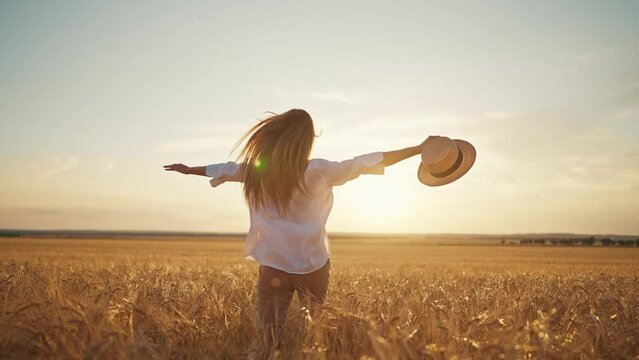 Romantic carefree happy woman running on yellow wheat field with spreading flying arms enjoying freedom calmness on rural nature during vacations holidays. Rest, relax in country, village at sunset.
