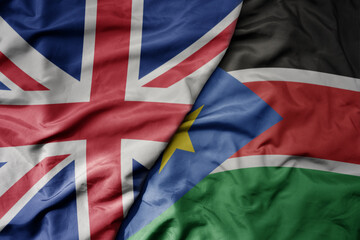 big waving national colorful flag of great britain and national flag of south sudan .