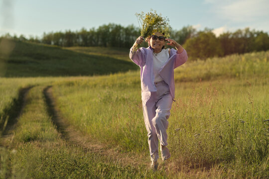 Energetic mature Asian woman enjoying nature, embodying vitality and health with a bouquet of flowers in her hands