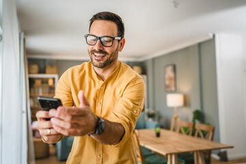 One adult man with eyeglasses stand at home use mobile phone