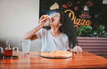 Lifestyle of afro-haired woman enjoying a pizza in a restaurant. Happy afro hair woman eating pizza in a restaurant