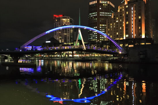 Night view of the Evan Walker-Southbank Pedestrian Bridge, high-rise buildings and green-illuminated tall spire. Melbourne-Australia-762