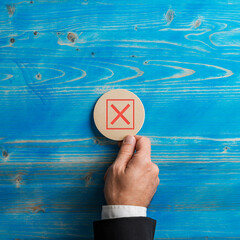 Hand of a businessman placing a wooden cut  circle with a red x sign on it over blue background