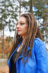 Portrait of a middle-aged woman in a blue leather jacket and dreadlocks. Woman posing in autumn park