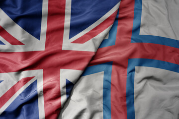 big waving national colorful flag of great britain and national flag of faroe islands .