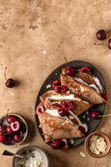 Chocolate Crepes with Cherry and Whipped Cream on brown textured background rustic style top view, flat lay with text space