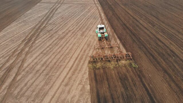 Agricultural Industry. Aerial view tractor with plough working on a field at sunset. Tractor plowing fields with a rotary plow on a large scale vegetable farm. Agriculture from above.