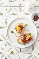 Bruschetta sandwiches with tomatoes, cream cheese, olive oil and basil on a plate on printed tile background, top view, copy space. Appetizer, italian antipasti