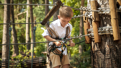 Little boy connecting his safety rope and hook before climbing up the tree in park