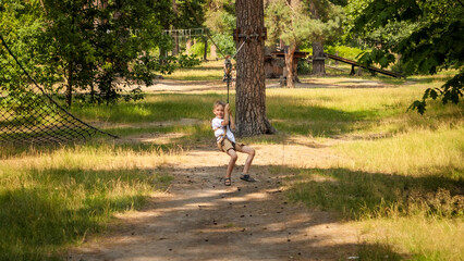 Happy laughing boy having fun riding on the zip line at summer park. Active childhood, healthy lifestyle, kids playing outdoors, children in nature. © Kyrylo Ryzhov