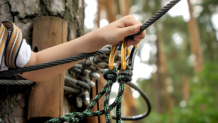 Closeup of child hand holding rope and safety hook for mountain climbing and alpinism