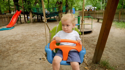 Closeup of cute baby boy sitting and swinging in colorful swing at park. Kids playing outdoors, children having fun, summer vacation and holiday.