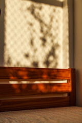 Abstract minimalist soft light background with light and shadow from the window and vegetation on the wall of a bedroom with wooden bed.