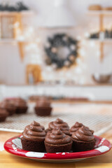 Chocolate cupcakes on a red plate on butcher block countertop in kitchen decorated for Christmas