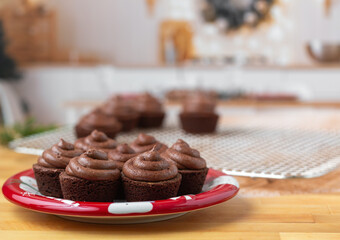 Chocolate cupcakes on a red plate on butcher block countertop in kitchen decorated for Christmas