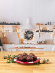 Chocolate cupcakes on a red plate on butcher block countertop in kitchen decorated for Christmas