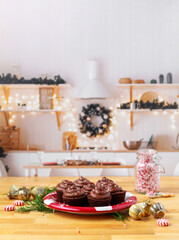 Chocoate Cupcakes with Peppermint Sprinkles on a red plate on butcher block countertop; kitchen decorated for Christmas in the background