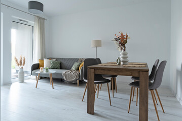 Living room with table and chairs in modern interior. Stylish apartment with window, white wall, sofa and wooden floor.