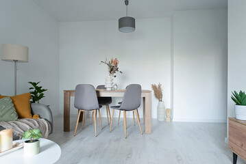 Living room with table and chairs in modern interior. Stylish apartment with white wall, sofa and wooden floor.