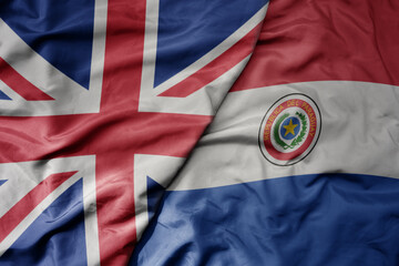 big waving national colorful flag of great britain and national flag of paraguay .