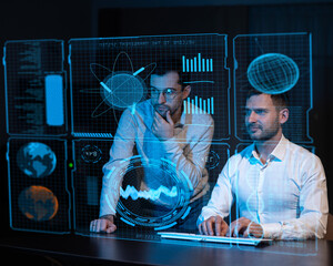Two caucasian bearded men look in the dark at a virtual screen. 
