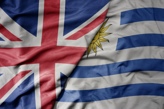 big waving national colorful flag of great britain and national flag of uruguay