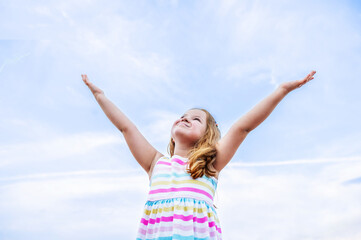 portrait of children, a happy smiling girl of 6 years old, against the background of a clear blue sky.the girl looks at the sky raised her hands up.Place for text. High quality photo