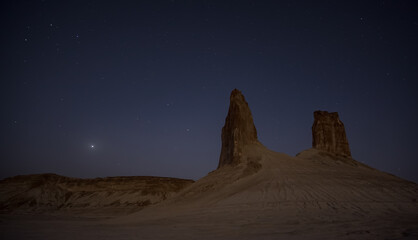 Chalk and limestone remnants in the Kazakh steppe at night against the background of the starry sky and the moon, vertical landforms after weathering in the desert