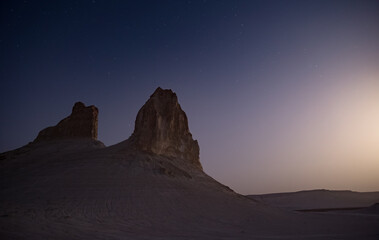 Chalk and limestone remnants in the Kazakh steppe at night against the background of the starry sky and the moon, vertical landforms after weathering in the desert