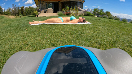 POV = POINT OF VIEW: Robotic mower is moving towards a lady sunbathing in garden