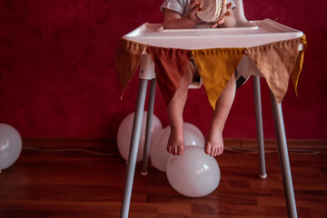 Faceless portrait of baby sitting in high chair, festively decorated with fabric pennants for party