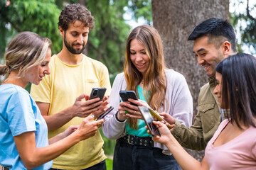 Multiethnic group with phones watching internet or social networks in the park, technology concept