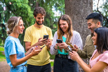 Multiethnic group smiling with phones on internet or social networks in the park, technology concept