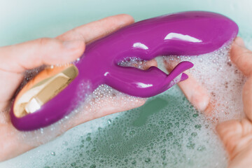 Hands washing sex toy vibrator with soapy foam