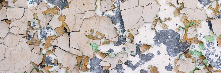 Peeling paint on the wall. Panorama of a concrete wall with old cracked flaking paint. Weathered rough painted surface with patterns of cracks and peeling. Panoramic texture for background and design.