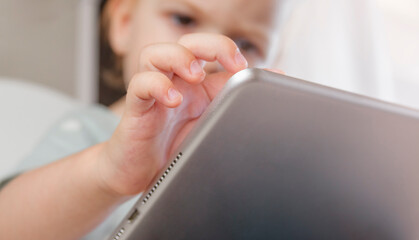 Little child plays with tablet sitting on highchair. Child hands with tablet