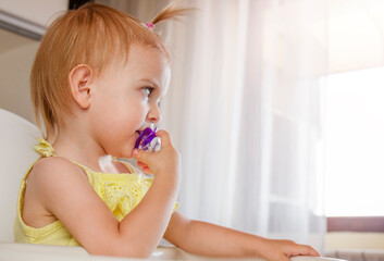 Toddler girl with pacifier sitting on highchair. Copy Space