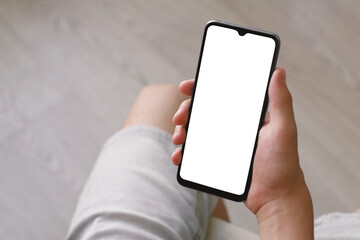 A teenager holds a smartphone with one hand. Phone with white screen on defocused light background. There is a work path in the file.