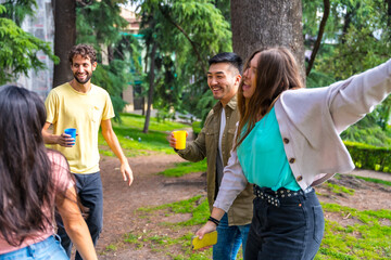 Multiethnic group of birthday party in the city park having fun and dancing with colored cups