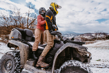 A young adventurous couple embraces the joy of love and thrill as they ride an ATV Quad through the snowy mountainous terrain