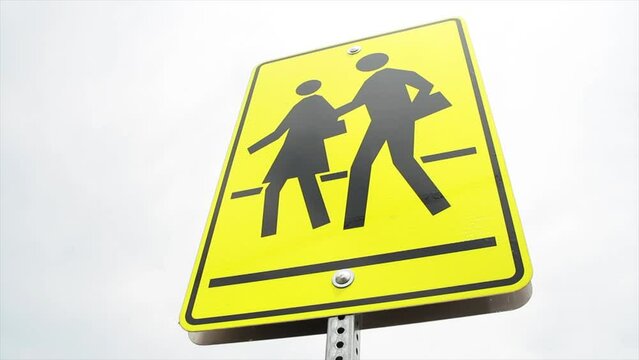 rectangle pedestrian school zone crossing sign, black print on yellow background, wide angle shot from low with sky in background